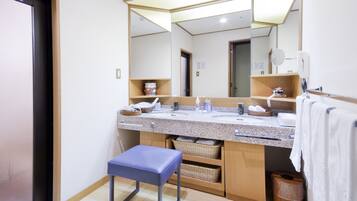 A modern bathroom with a large mirror, two sinks, a blue bench, and storage baskets.