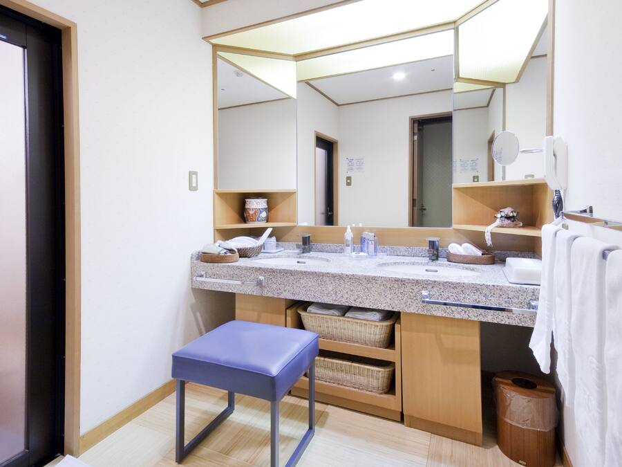 Un baño moderno con un espejo grande, dos lavamanos, un banco azul y cestas de almacenamiento.