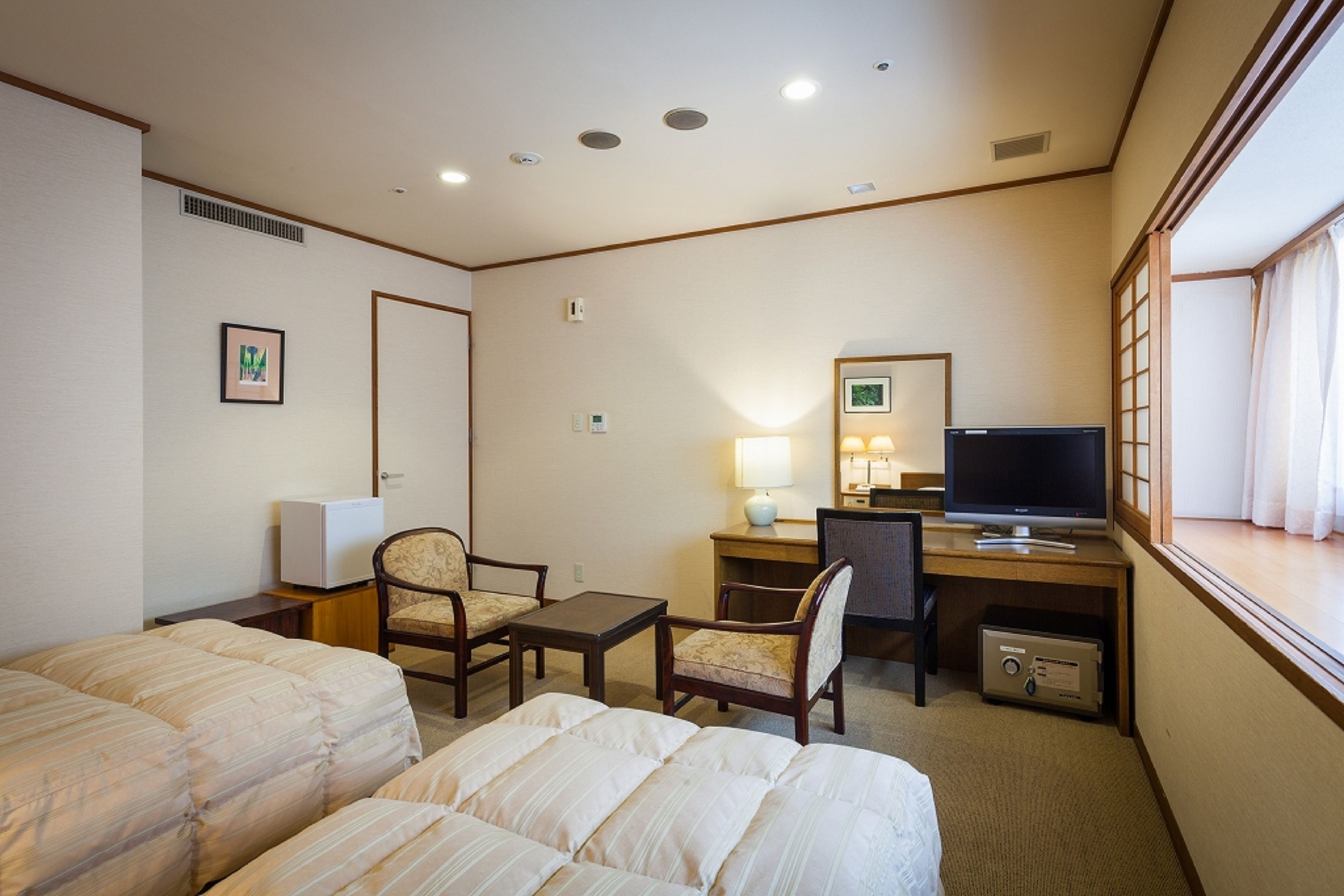A hotel room with two beds, a desk with a computer, a TV, and a window with curtains.