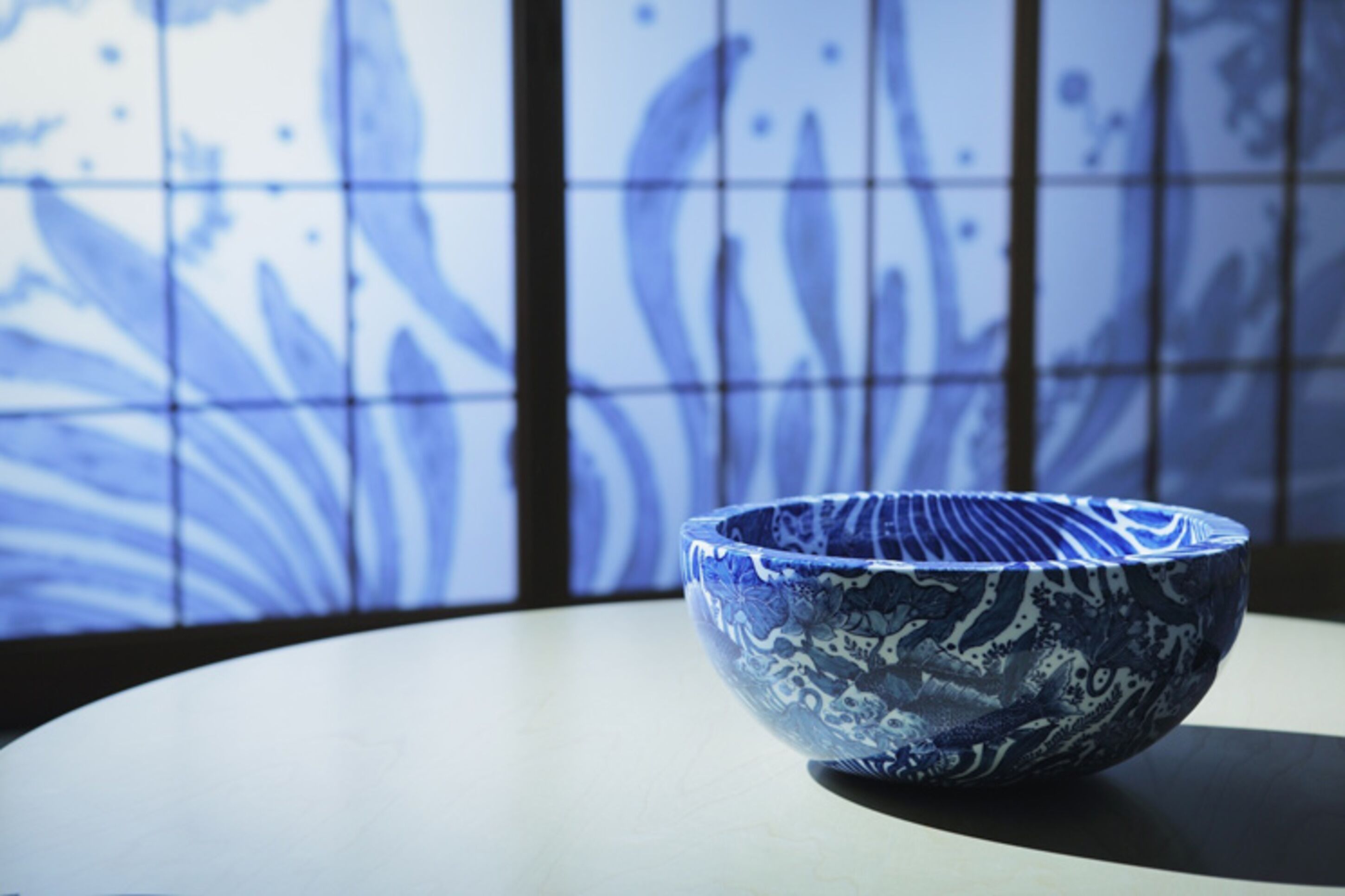 A blue ceramic bowl on a table with a tiled wall in the background.