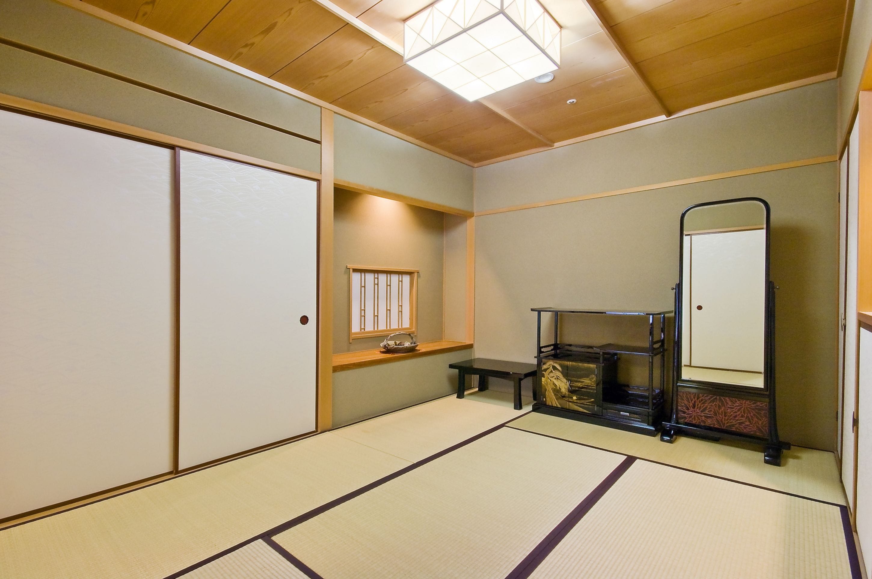 Ein traditioneller japanischer Raum mit Tatami-Boden, Schiebetüren, einer kleinen Sitzbank und einem Regal mit Spiegel.