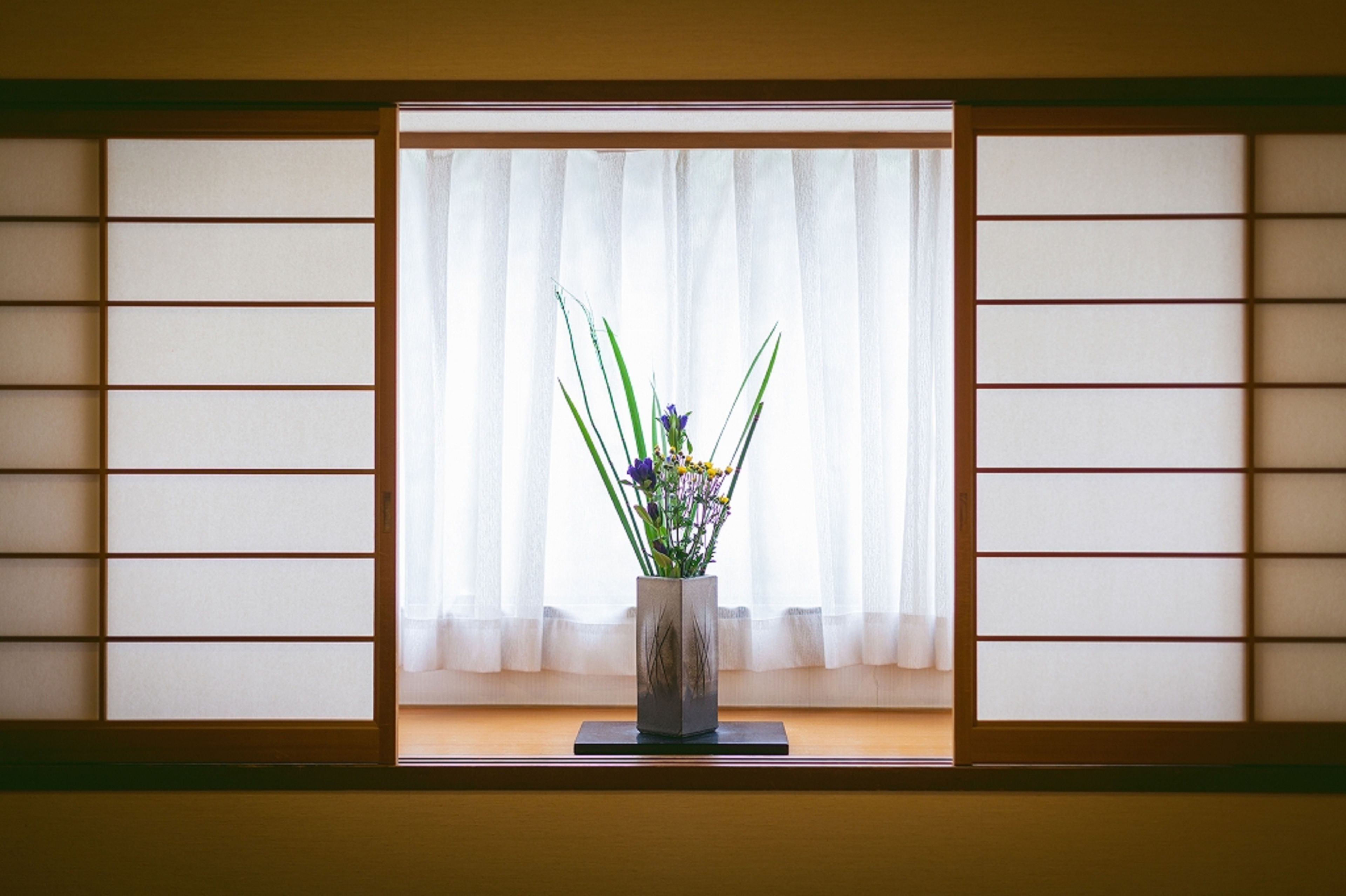 A traditional Japanese room with tatami flooring, a shoji screen, and a vase of flowers on a table.