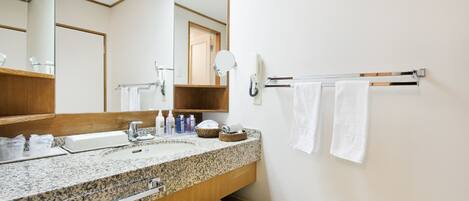 A modern bathroom with a granite countertop sink, a large mirror, a towel rack with two white towels, and a wicker stool.