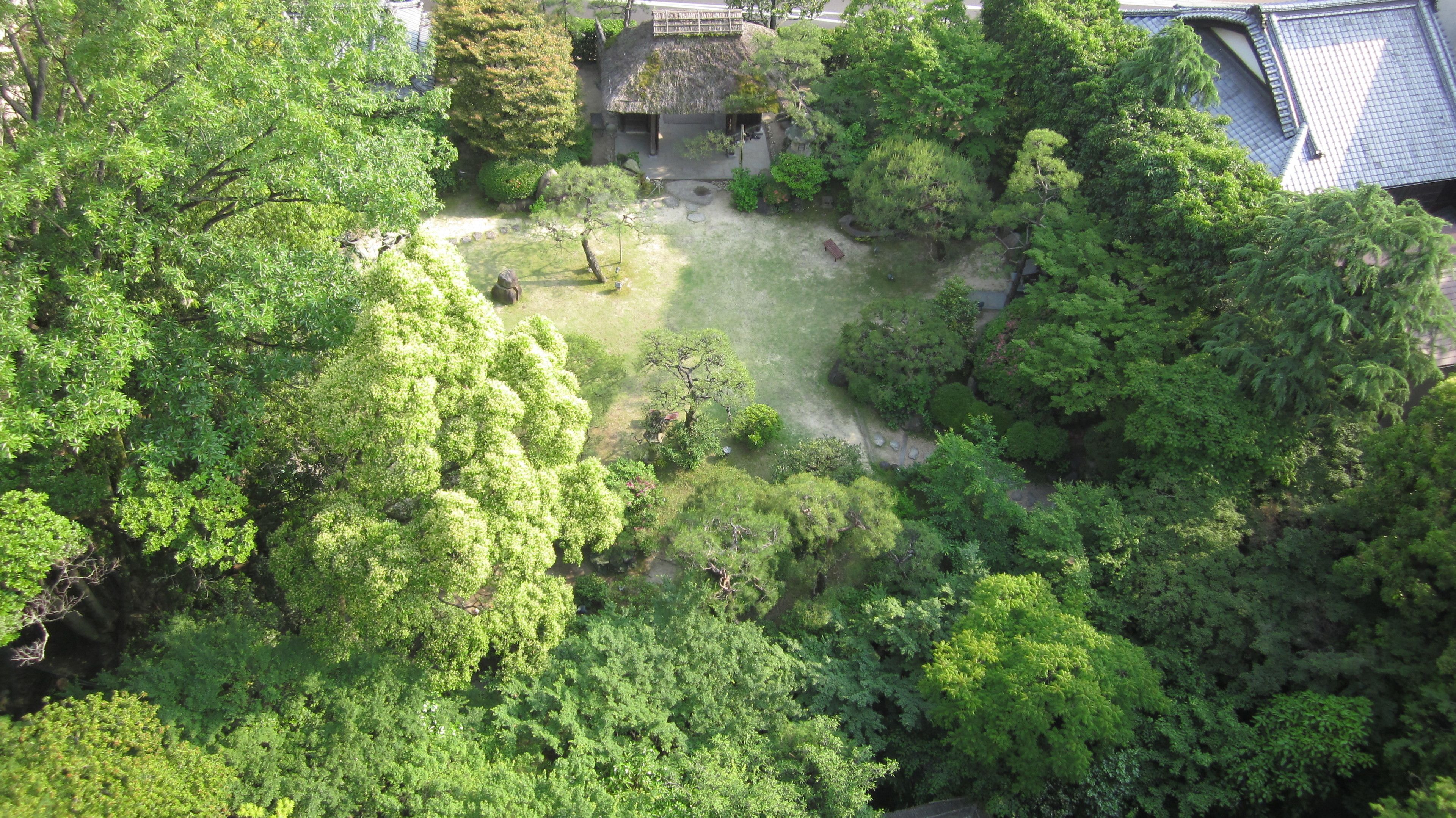 An aerial view of a lush green park with a traditional Japanese-style building, surrounded by dense foliage.