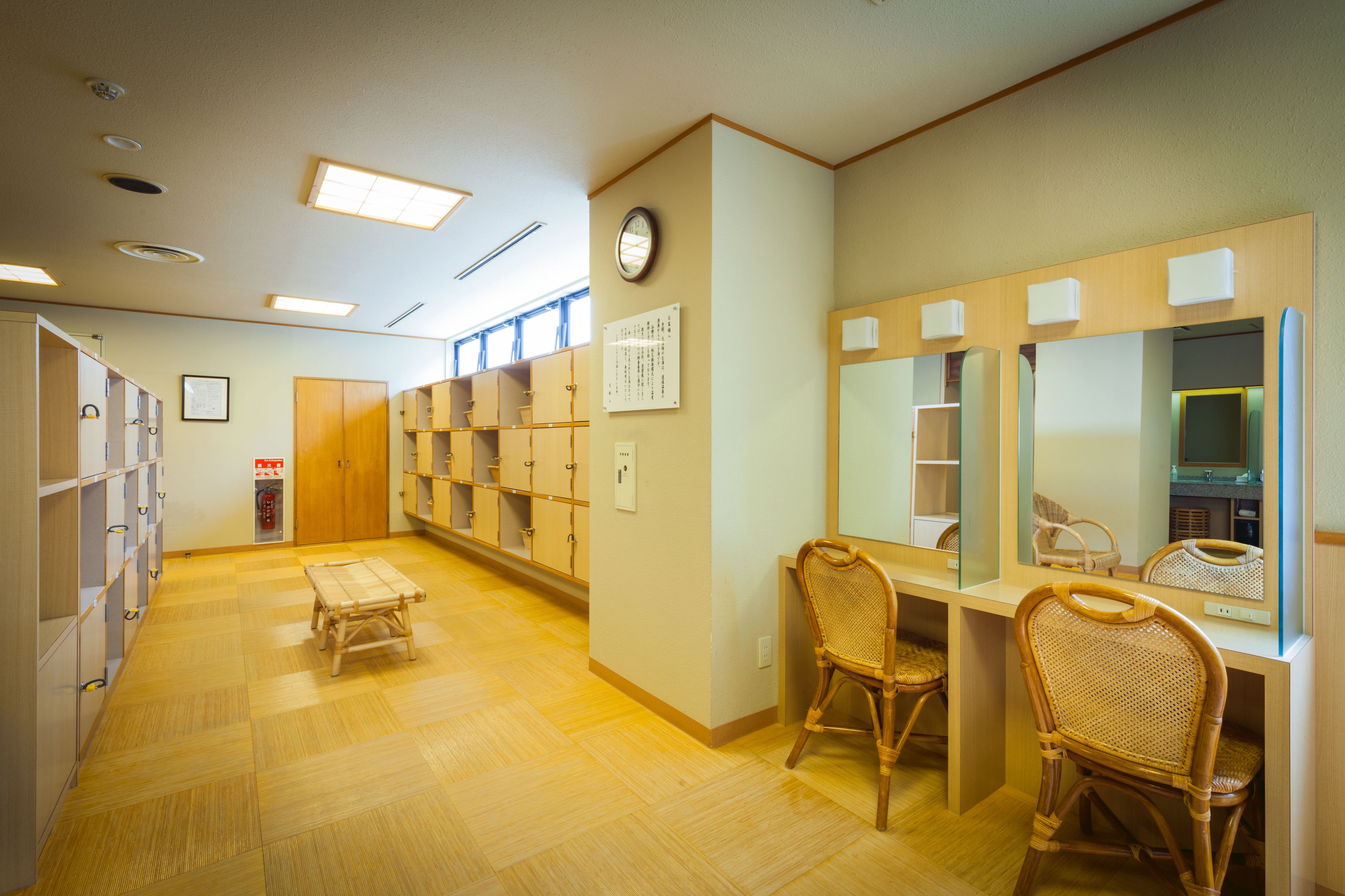A hotel room with a wooden floor, a desk with chairs, a mirror, and a wardrobe with shelves.