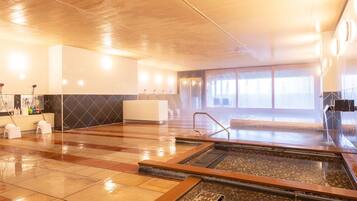 Amplia zona de piscina interior con varias pistas de natación, un mostrador de recepción y un ventanal que proporciona luz natural.