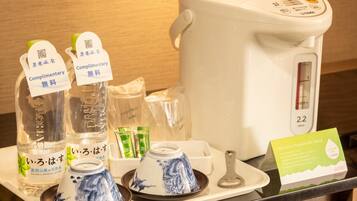 A hotel room's minibar with bottled water, a tea set, a kettle, and a welcome card.