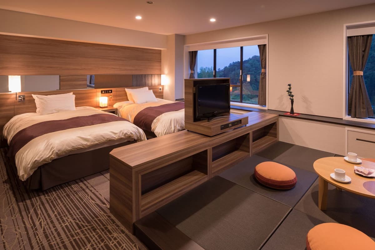 Ett hotellrum med två sängar, en tv, ett litet bord och ett fönster med utsikt över träd.