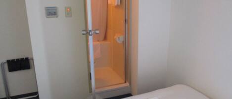 Habitación de hotel con cama, zona de ducha y perchero con colgadores.
