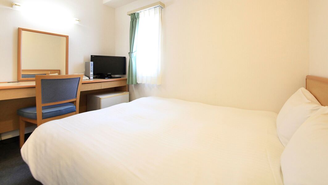 A hotel room with a bed, a desk with a computer, a chair, and a window with curtains.