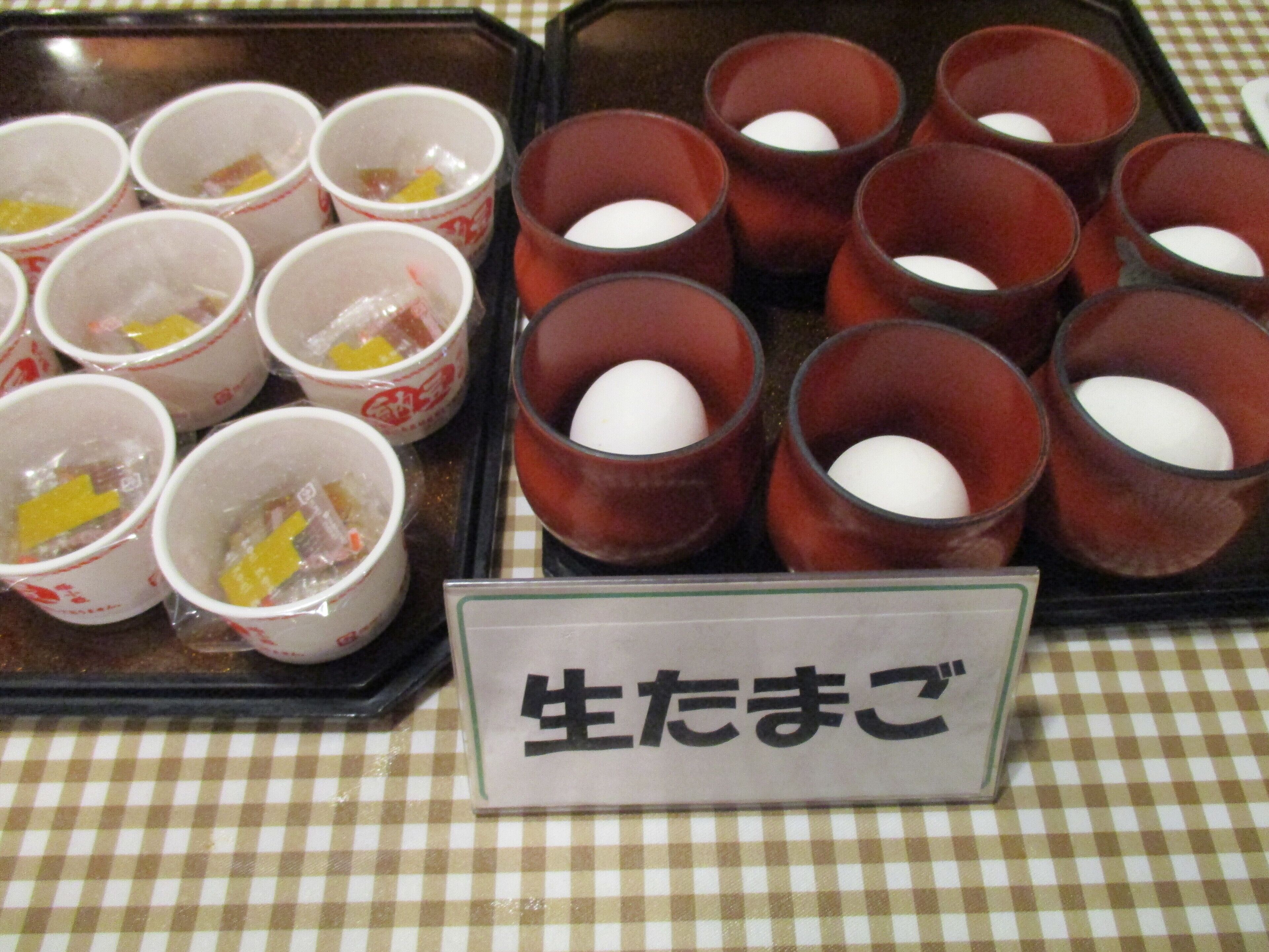 Uma bandeja com diversos copos contendo alimentos, alguns com gemas de ovo visíveis, e uma placa com texto em japonês.