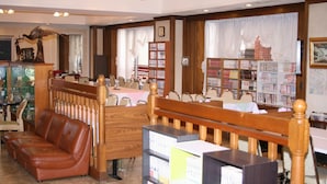 A library with wooden furniture, bookshelves, and a brown leather couch. - Fukui Palace INN (Fukui)