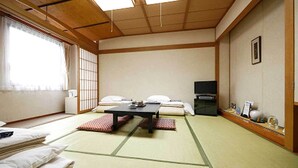 A traditional Japanese room with tatami flooring, a low table, futon beds, a television, and a sliding door. - Hotel Fukui Castle (Fukui)