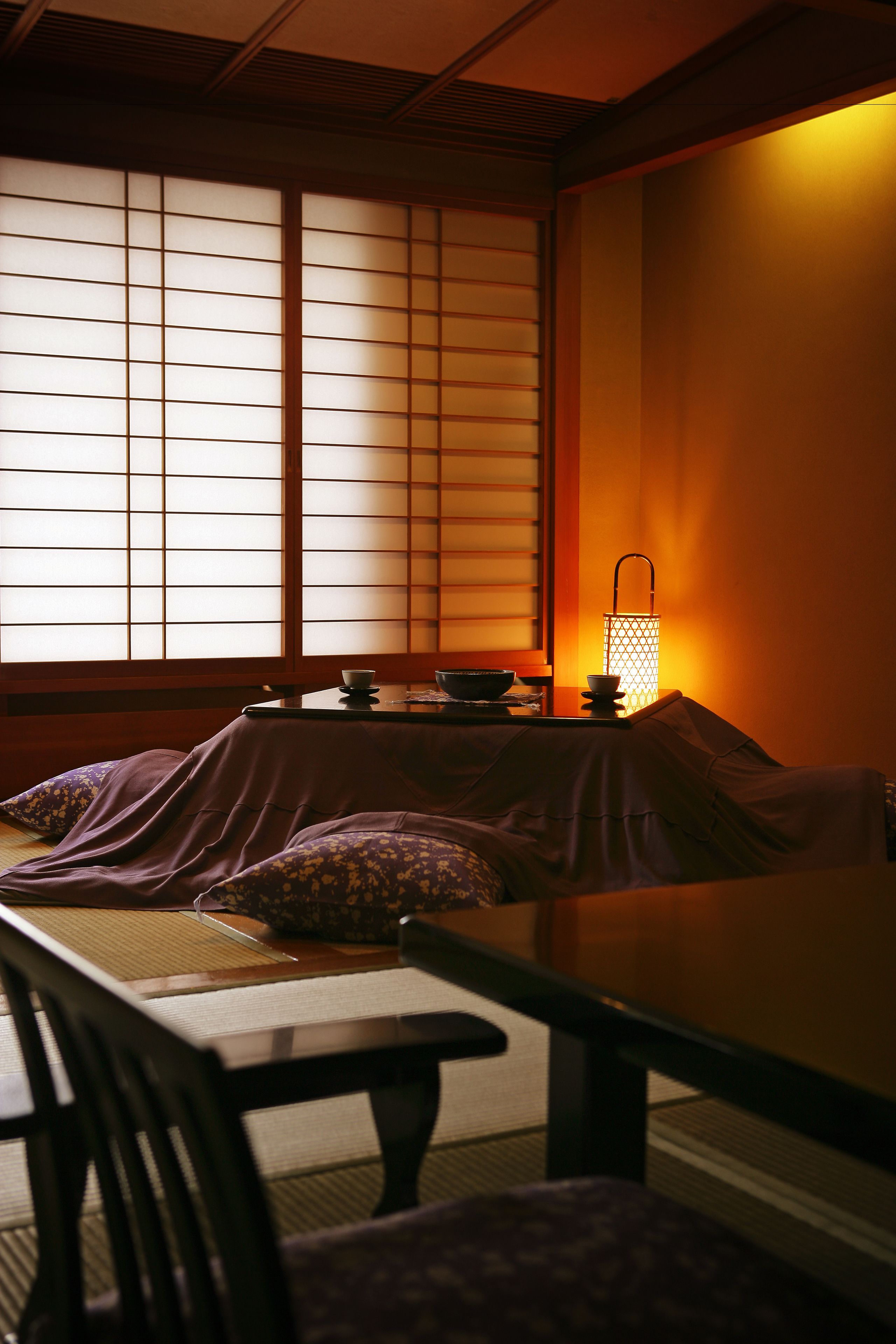 A traditional Japanese room with tatami flooring, a low table, and a lantern providing warm light.