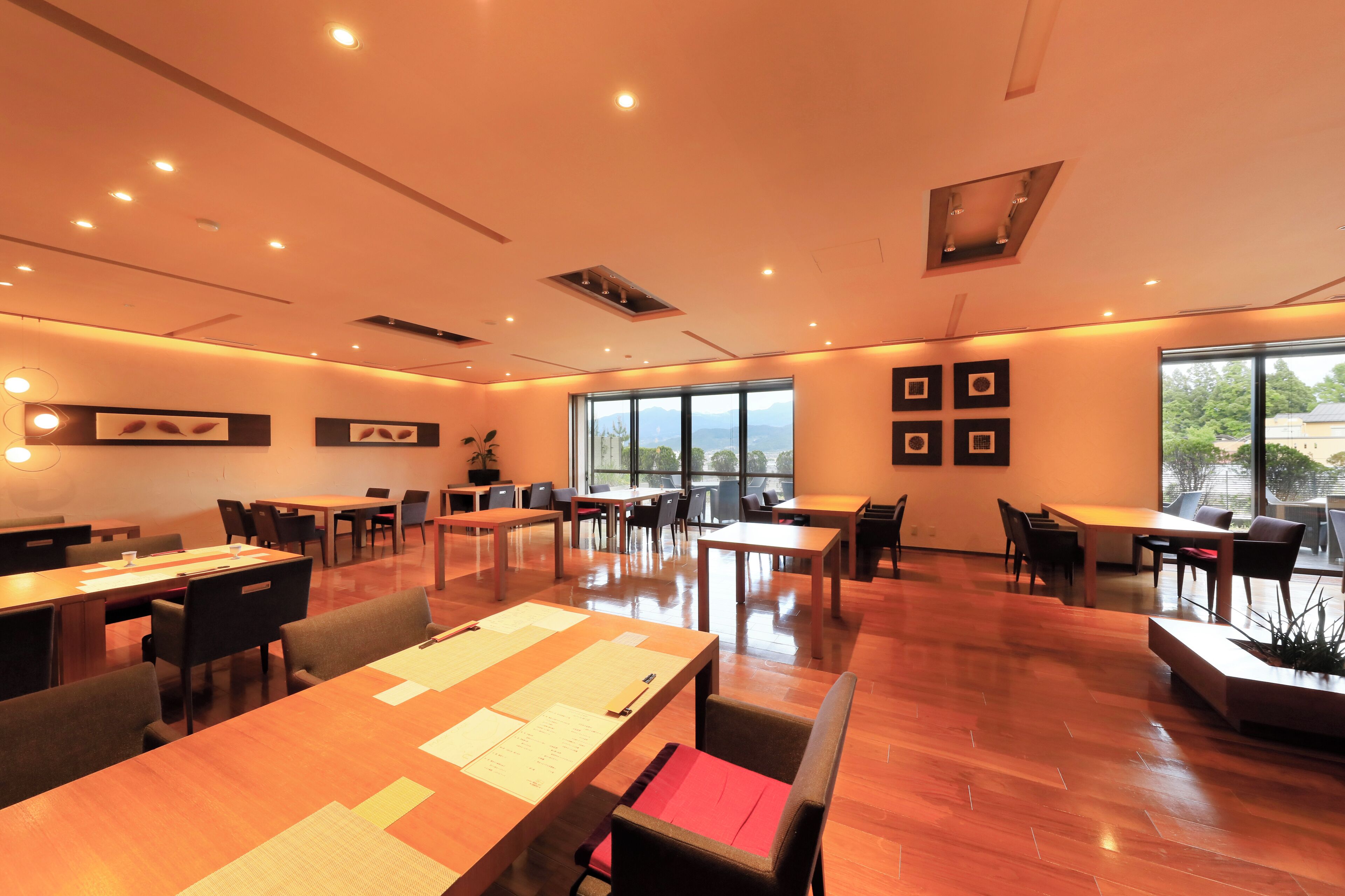 A modern conference room with wooden tables, chairs, and a large window providing a view of the outdoors.