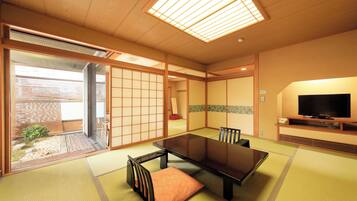 Una habitación japonesa tradicional con suelo de tatami, una puerta corredera, un televisor y una mesa baja con sillas.