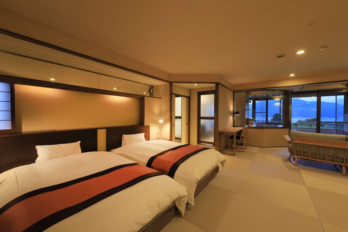 A hotel room with two beds, a desk, a chair, and a sofa.