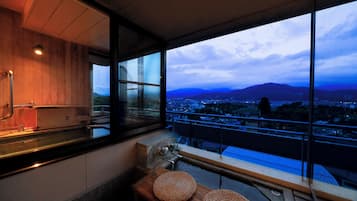 Un baño moderno con un tocador de madera, un lavamanos y un amplio ventanal con vistas a un paisaje urbano y montañas.