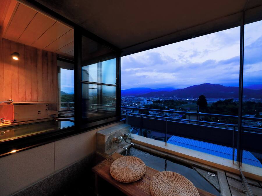 Un baño moderno con un tocador de madera, un lavamanos y un amplio ventanal con vistas a un paisaje urbano y montañas.