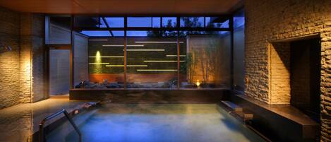 A modern spa with a heated pool, stone walls, and large windows.
