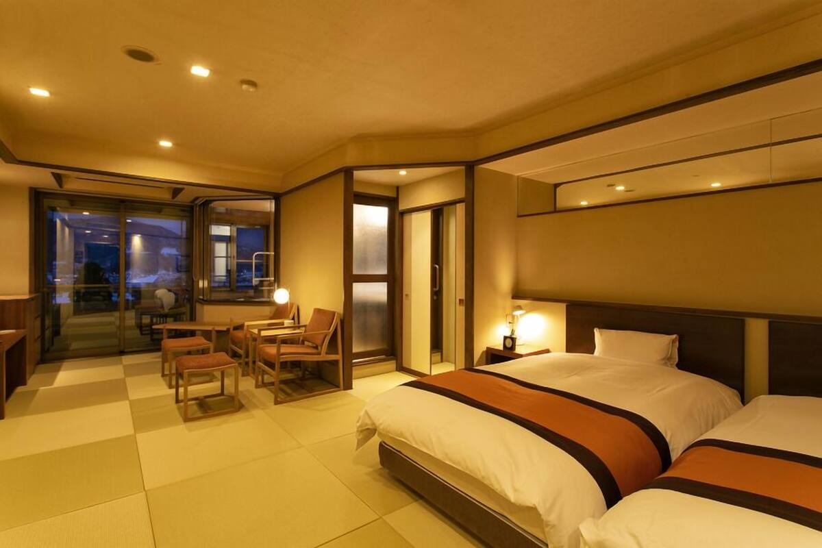 A hotel room with a bed, bedside tables, a desk with chairs, and a view through a glass door.