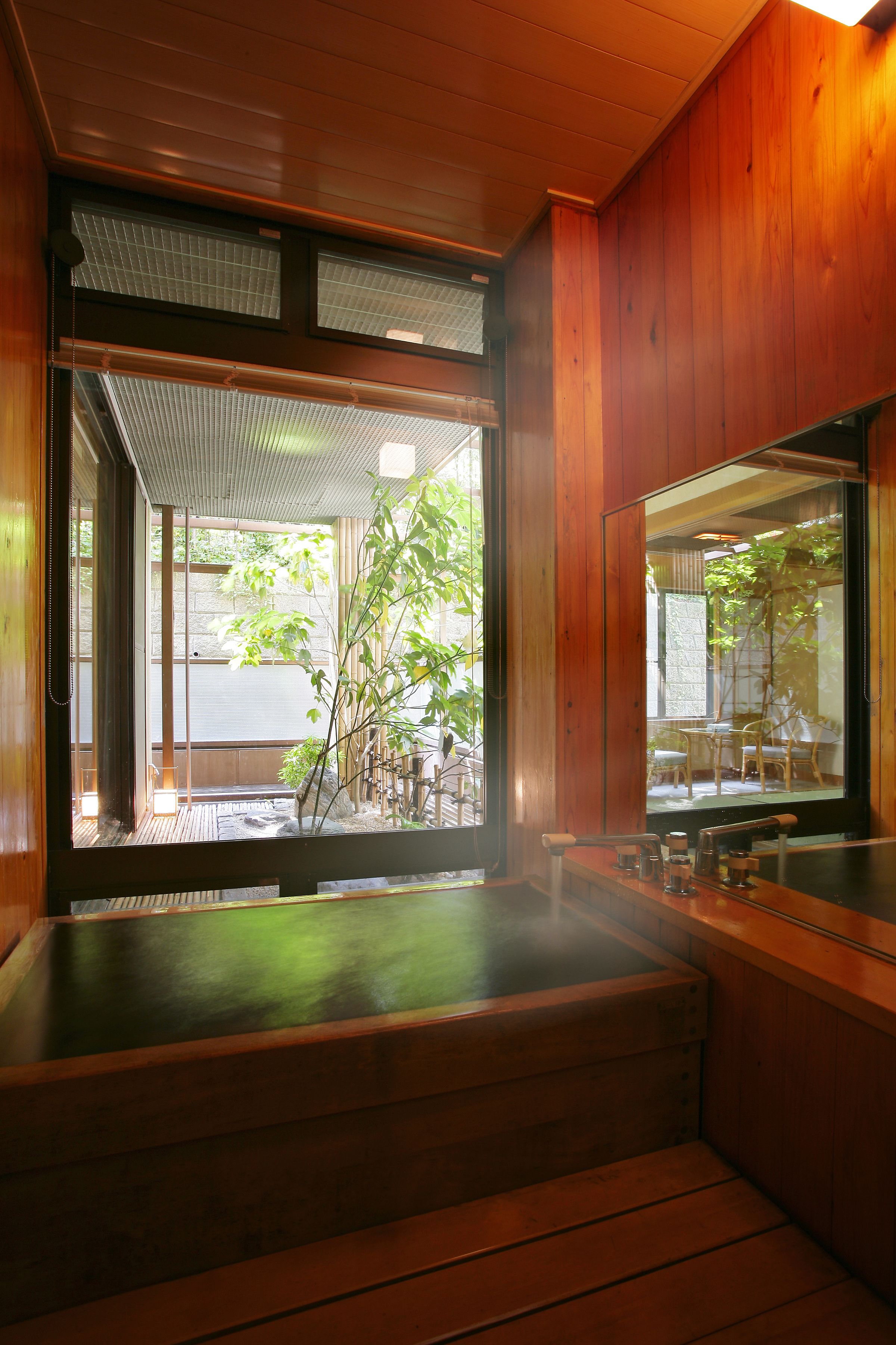 A traditional Japanese-style room with a wooden interior, a hot spring bath, and a view of a bamboo garden.