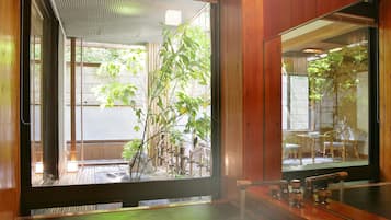 A traditional Japanese-style room with a wooden interior, a hot spring bath, and a view of a bamboo garden.