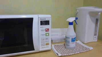 A microwave, a spray bottle, and a kettle on a wooden surface.