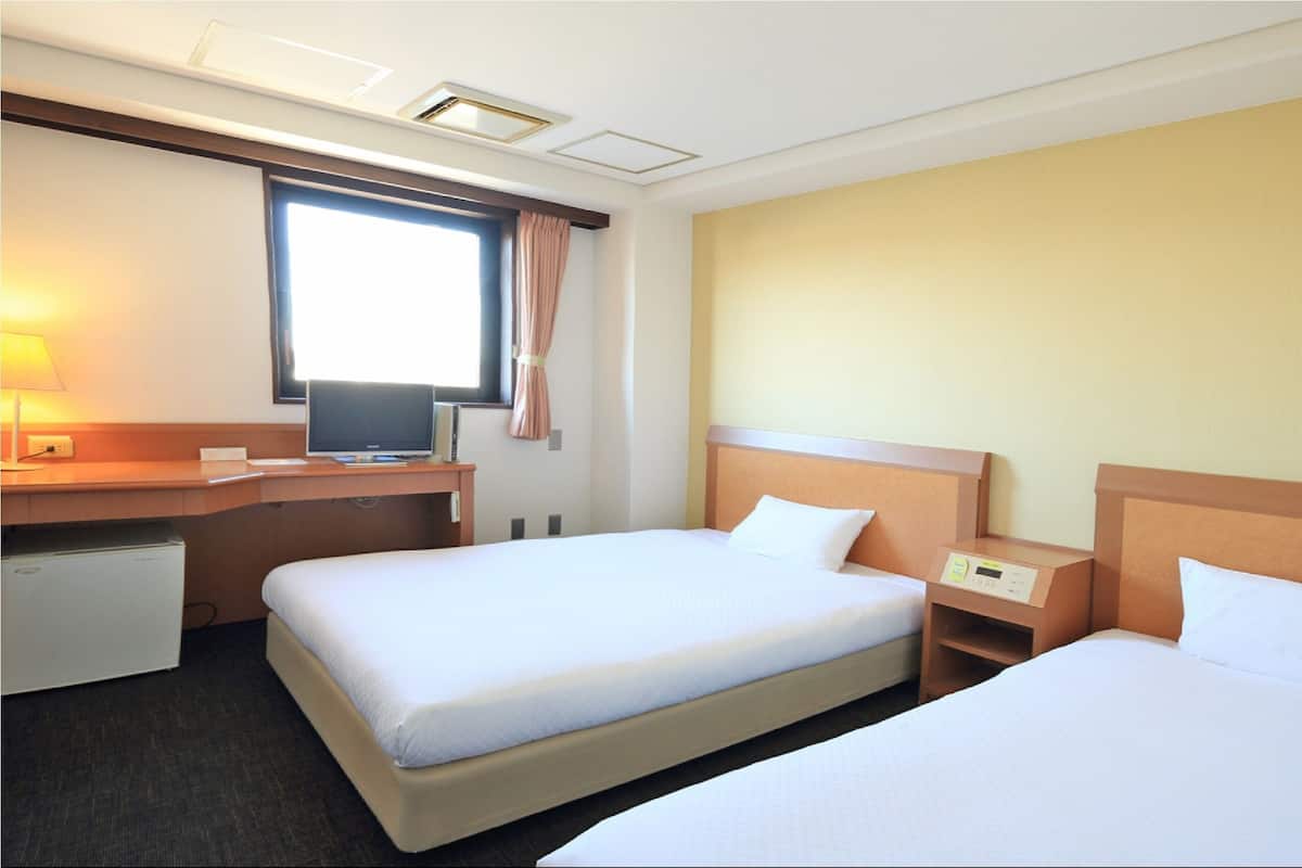 A hotel room with two beds, a desk with a computer, a small refrigerator, and a window with curtains.
