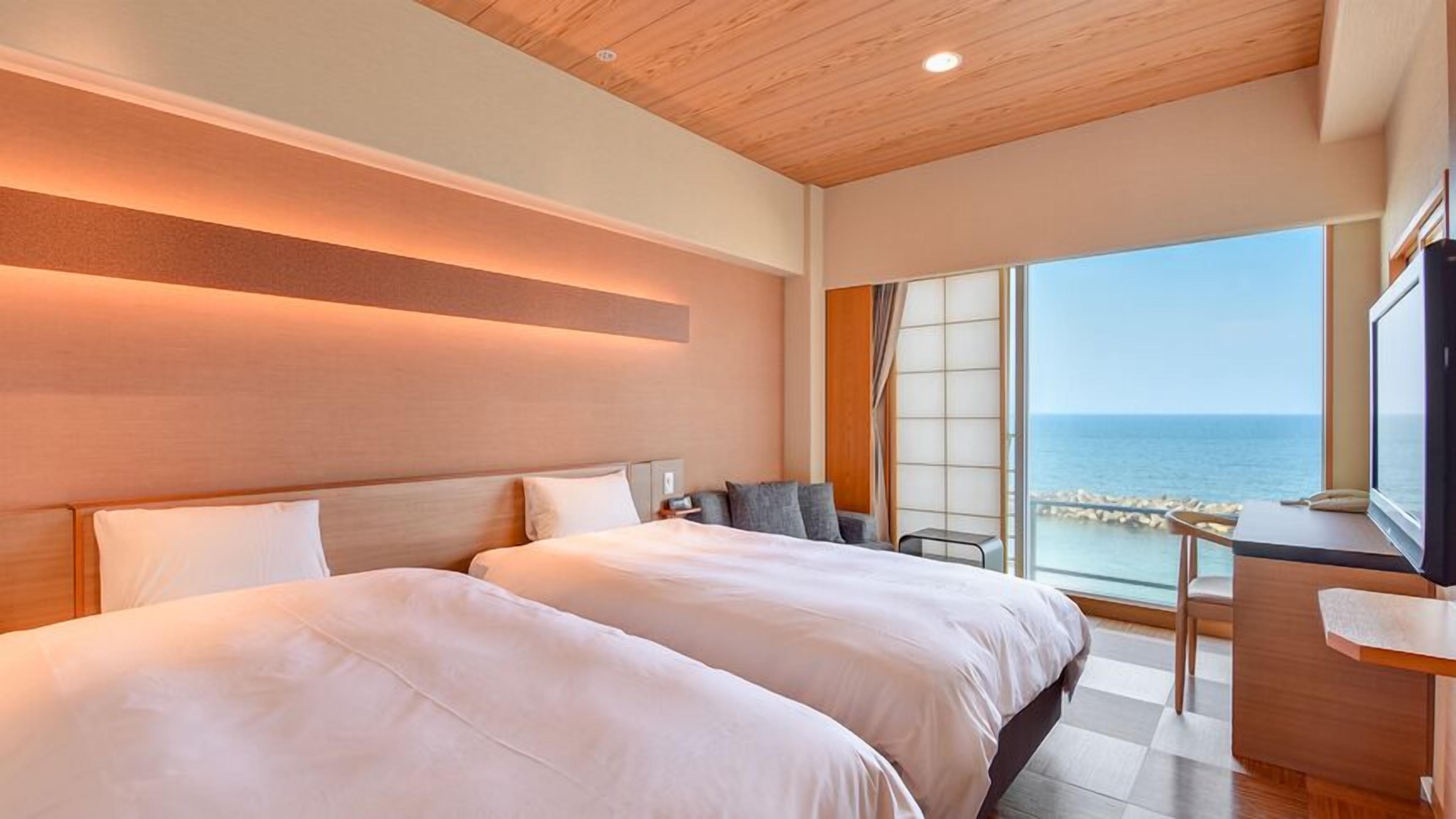 Ett hotellrum med två sängar, ett skrivbord och utsikt över havet.