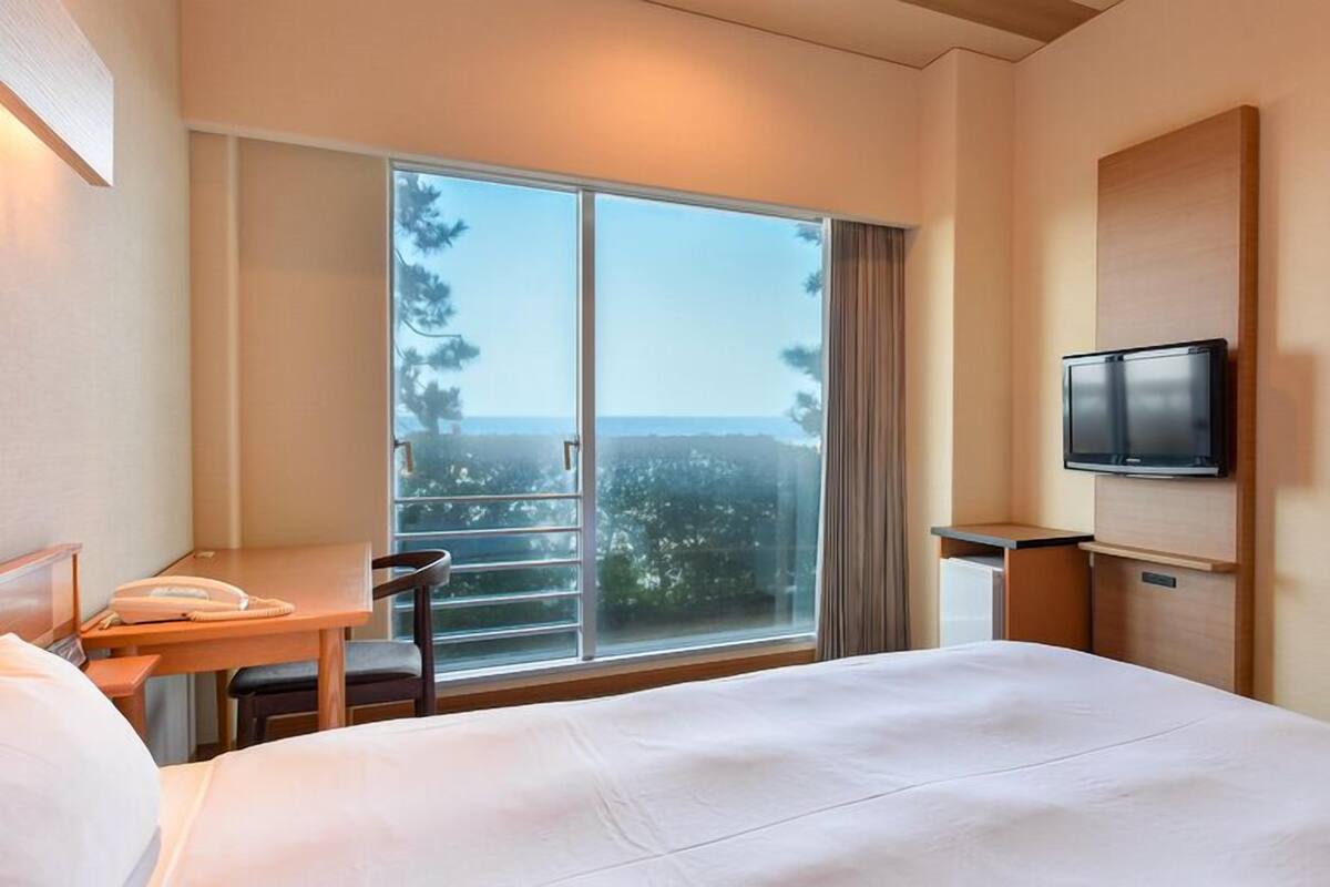 A hotel room with a large bed, a desk with a telephone, a television, and a balcony with a view.