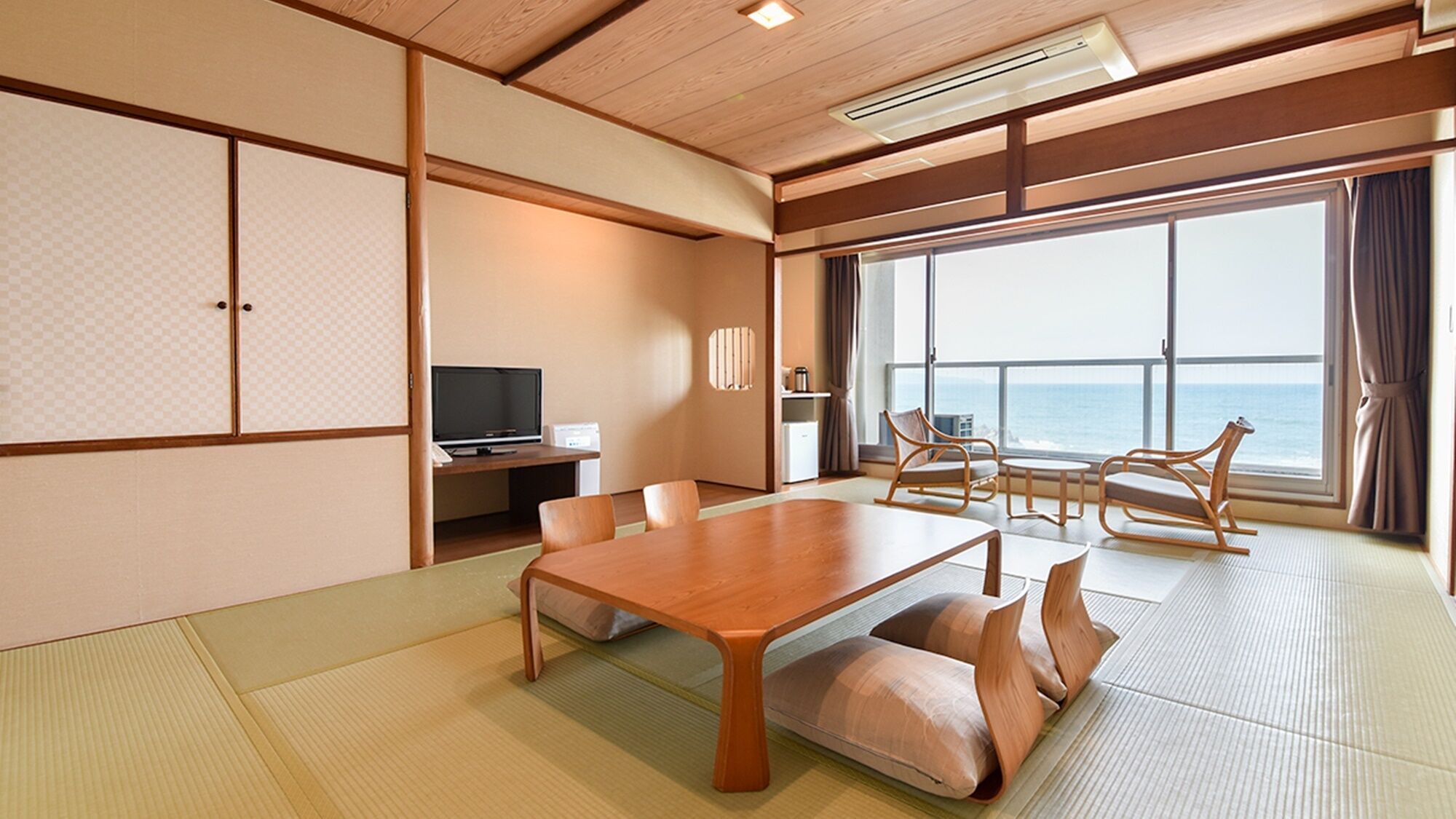 Ett traditionellt japanskt rum med tatamimattor på golvet, ett träbord, stolar, en tv och utsikt över havet.