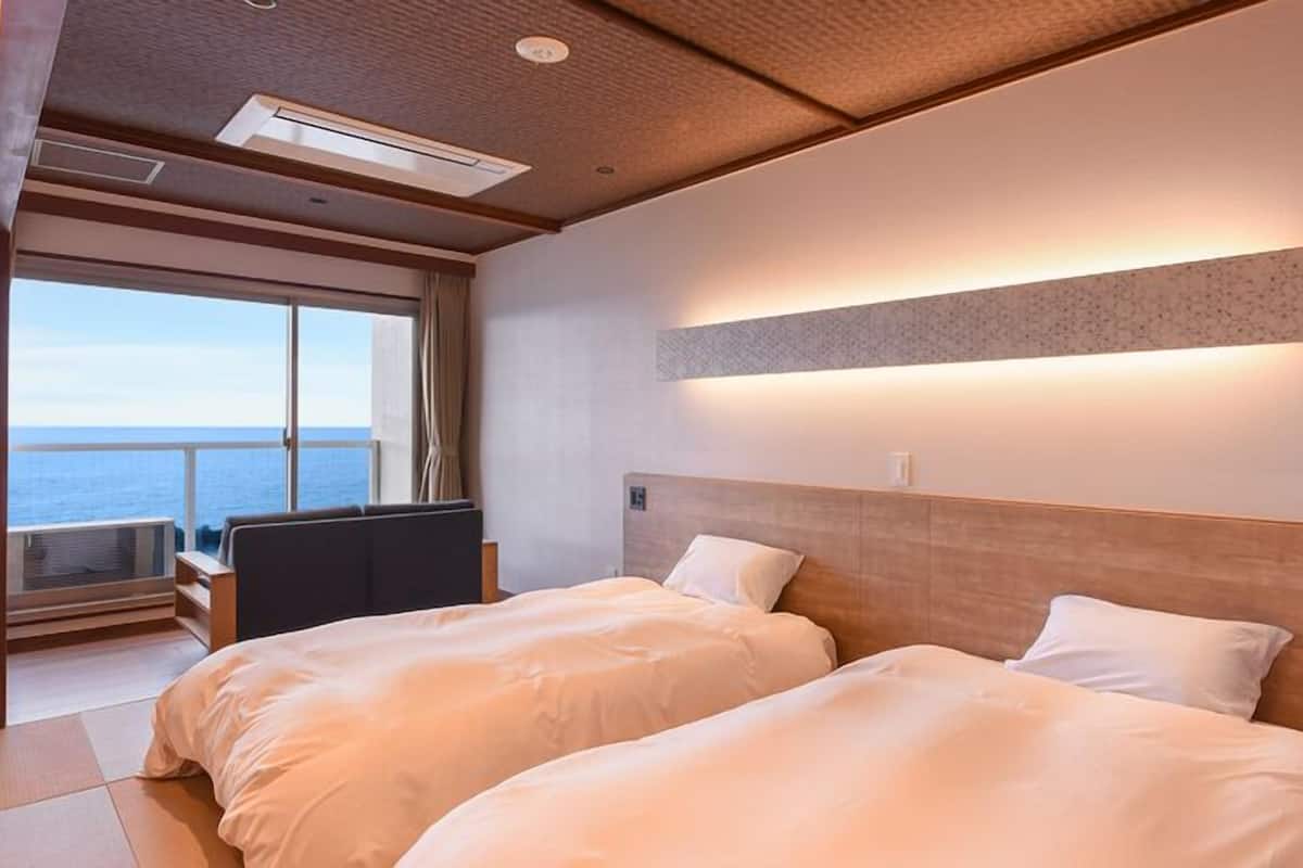 Ett hotellrum med två sängar, ett skrivbord och ett stort fönster med utsikt över havet.
