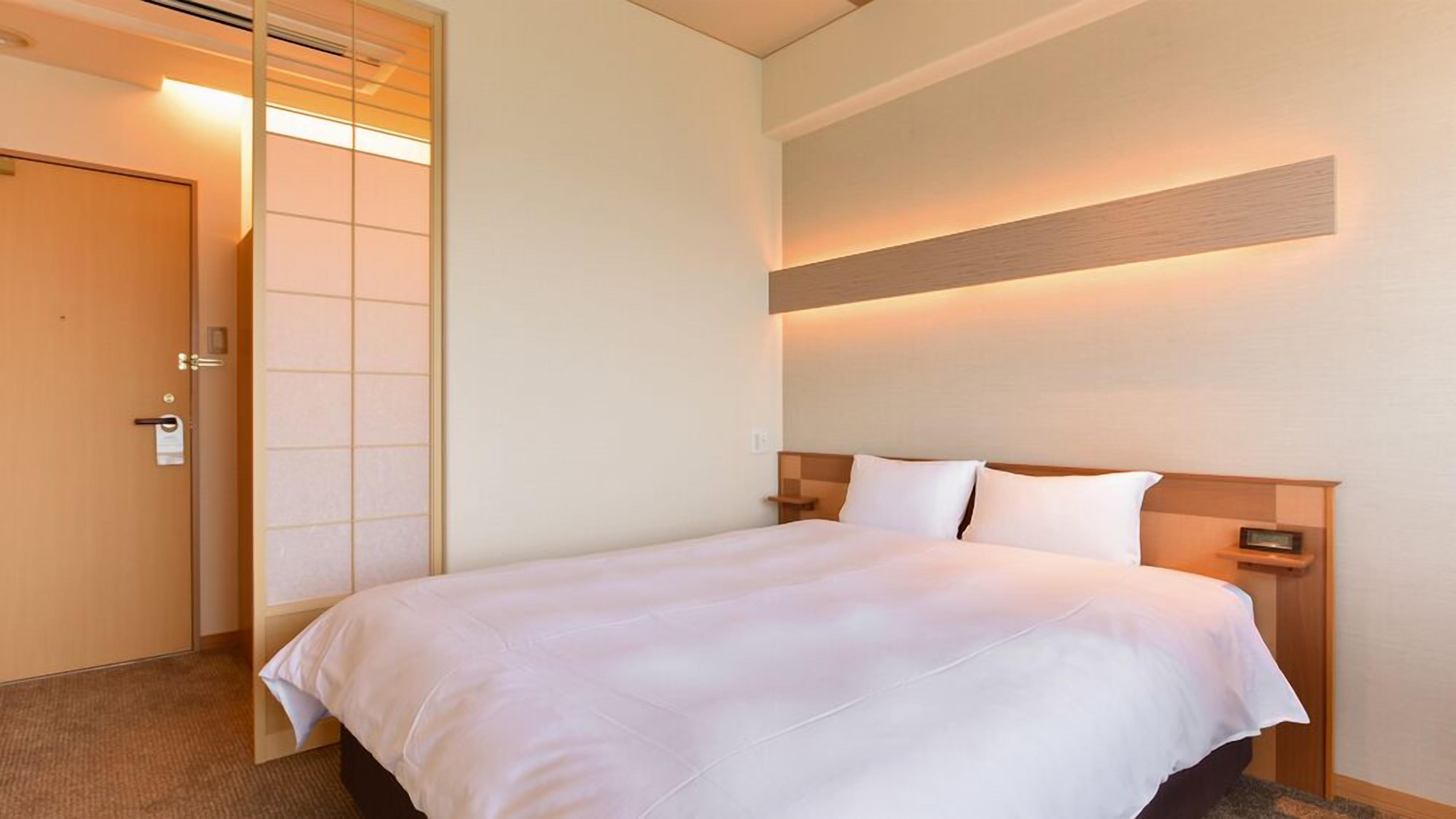 Ett hotellrum med en säng, sängbord, en väggmonterad lampa och en dörr med en skjutpanel.