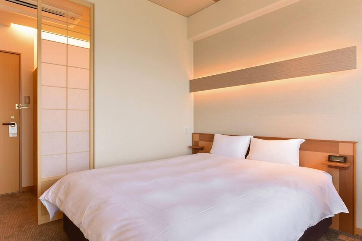 A hotel room with a bed, bedside tables, a wall-mounted light, and a door with a sliding panel.