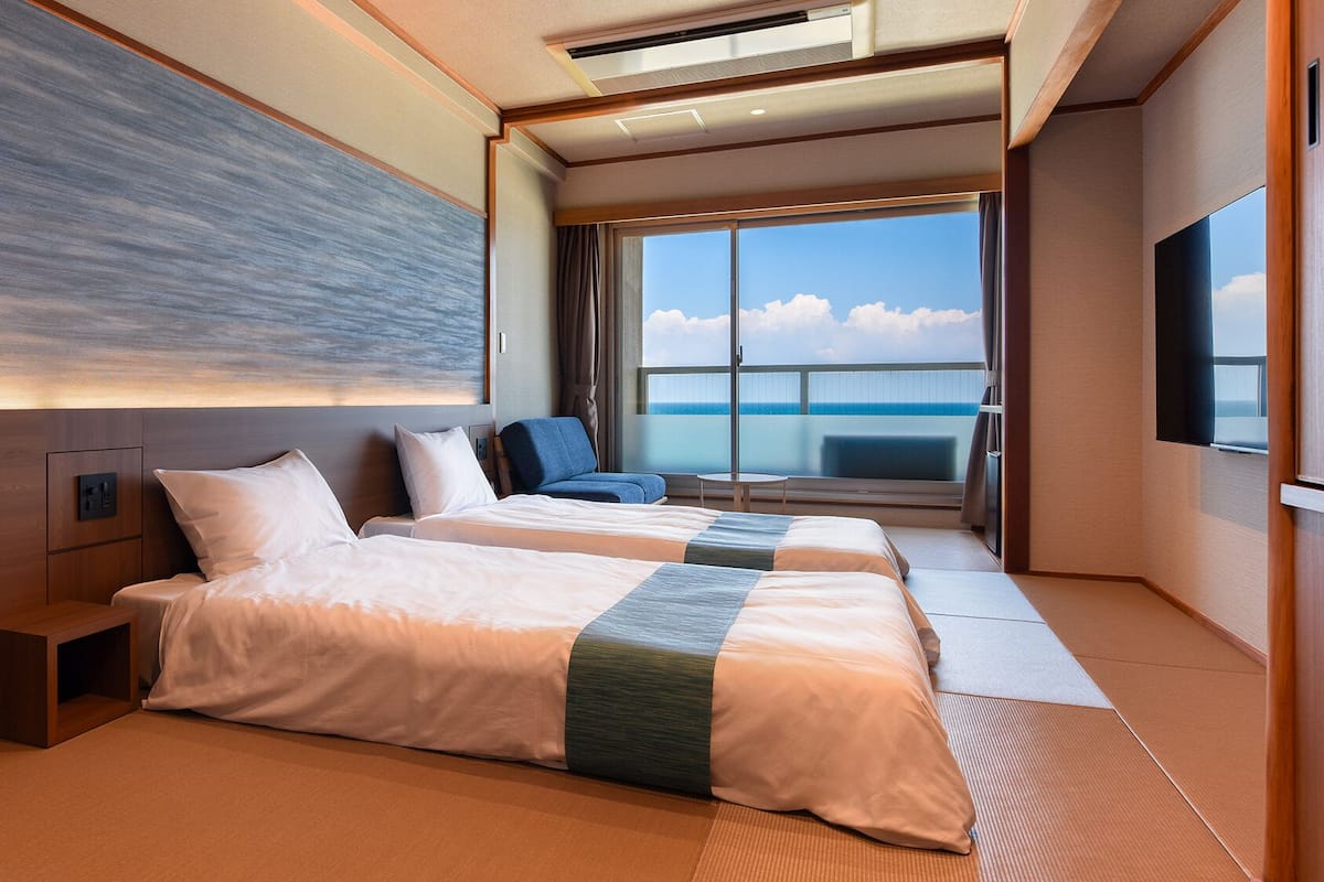 A hotel room with two beds, a large window with a view, and a flat-screen TV.