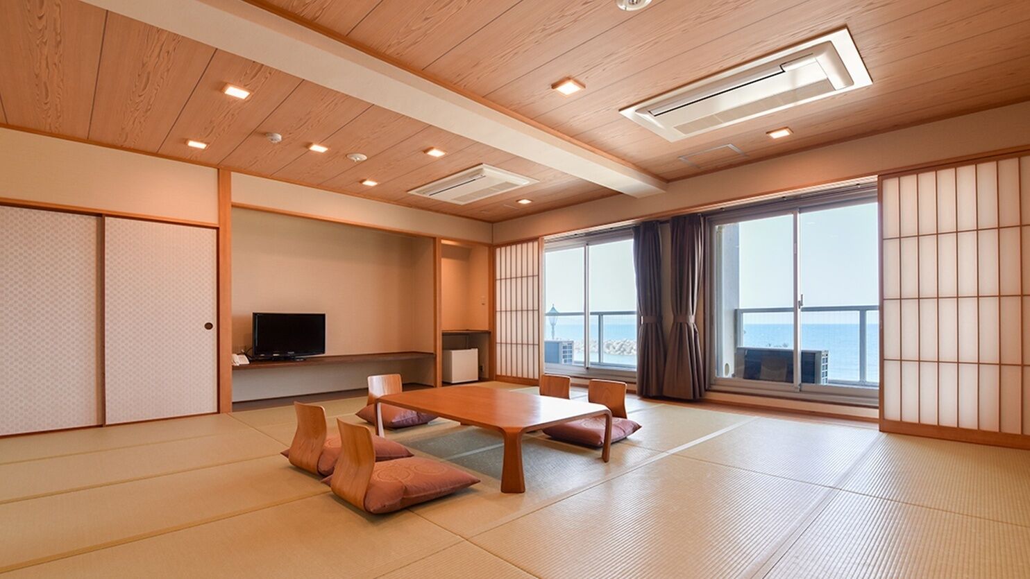Ett traditionellt japanskt rum med tatamimattor på golvet, ett lågt bord, kuddar, skjutdörrar och en tv.