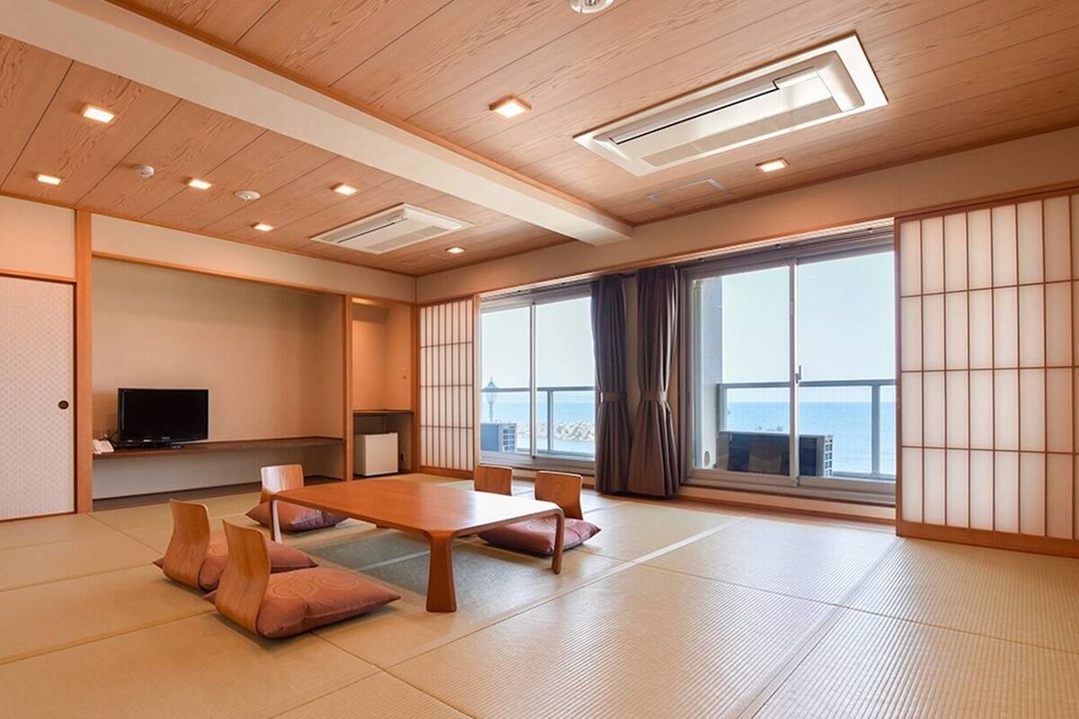 A traditional Japanese room with tatami flooring, a low table, cushions, sliding doors, and a television.