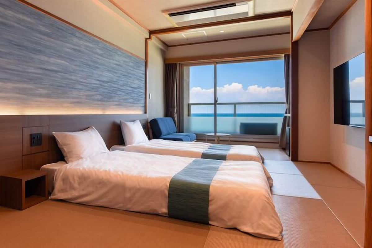 Ett modernt hotellrum med två sängar, ett stort fönster med utsikt över havet och en platt-TV.