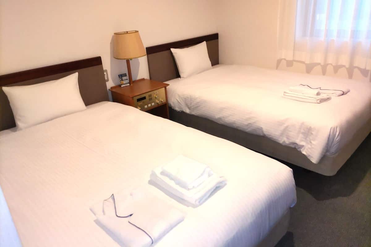 Two single beds with white linens, a bedside table with a lamp, and a window with curtains.