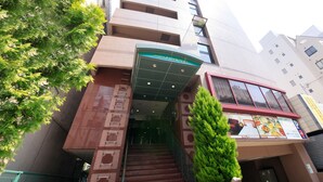 Entrada de hotel con toldo verde, una escalera que sube y un edificio alto al fondo.