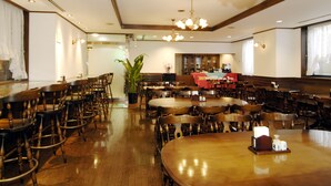 Un comedor amplio con varias mesas y sillas de madera, una planta central y una zona de bar con mantel rojo.