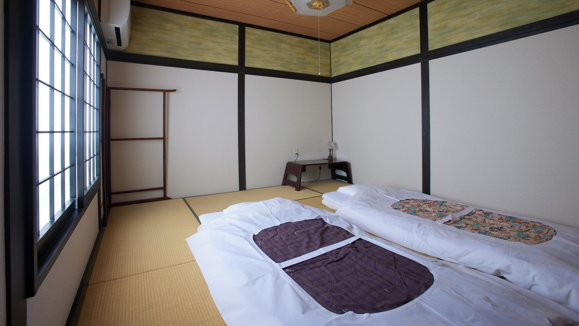 A room with tatami mat flooring, two beds with white bedding, a small desk, and a ladder against the wall.