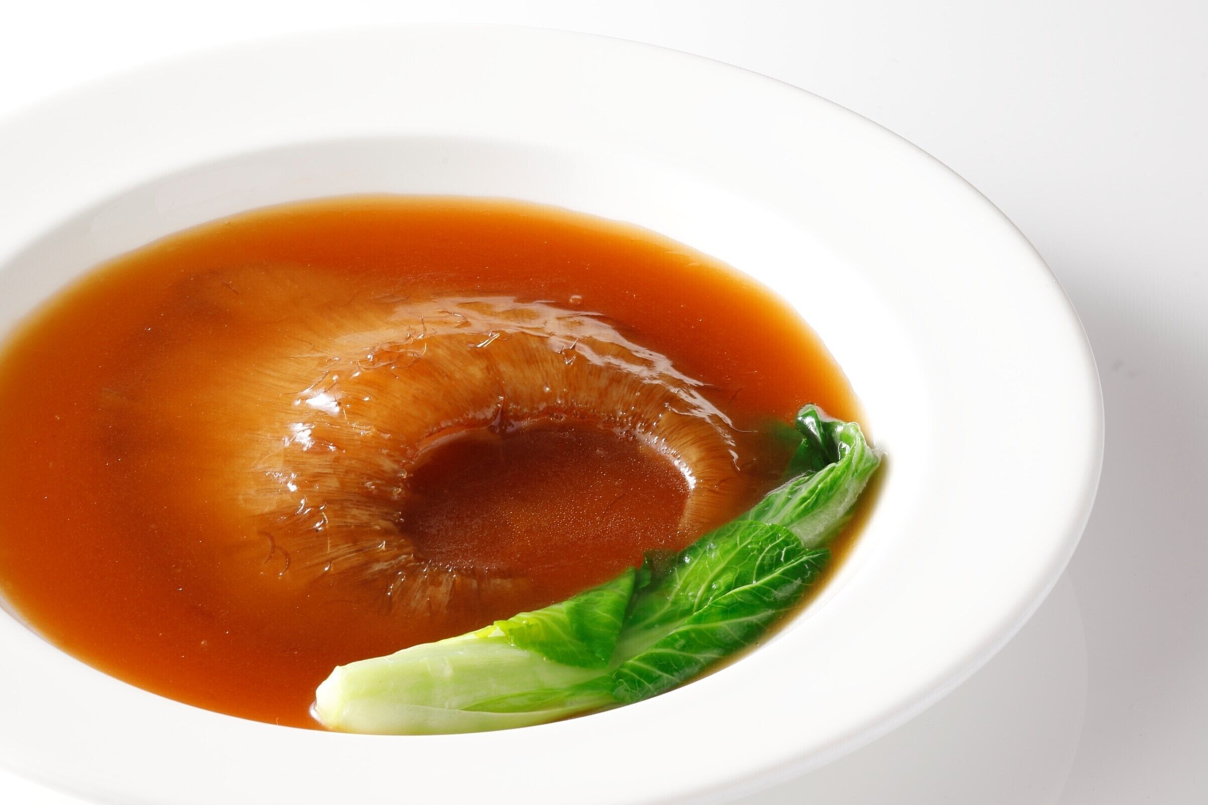 A bowl of soup with a clear broth and a piece of leafy vegetable.