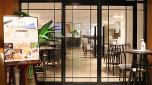Interior de restaurante con una pizarra de menú, mesas, sillas y una planta.