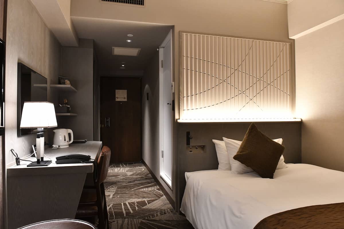 Une chambre d’hôtel avec un lit, un bureau doté d’une lampe, une machine à café et une moquette à motifs.