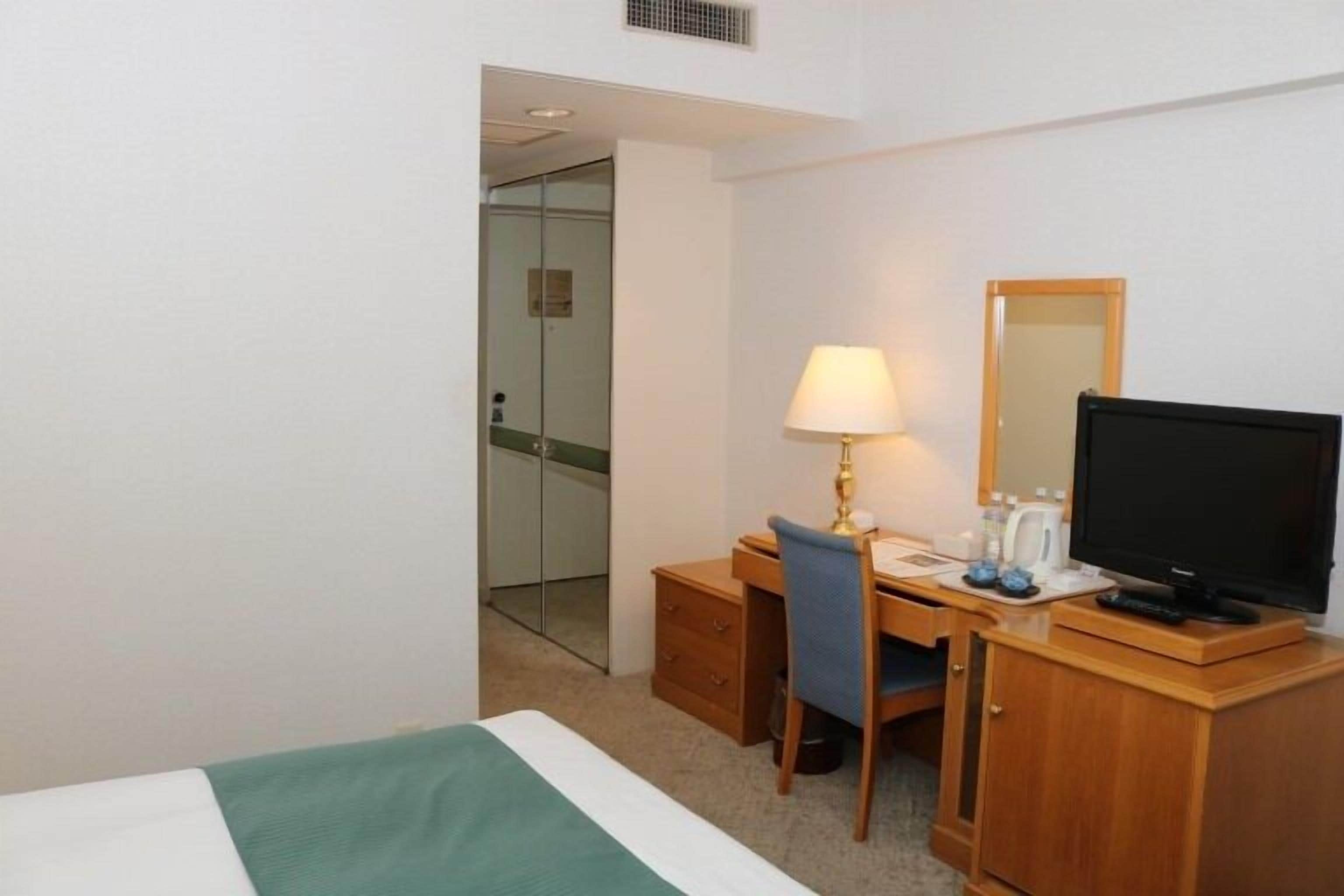 A hotel room with a bed, a desk with a chair, a television, and a mirror.