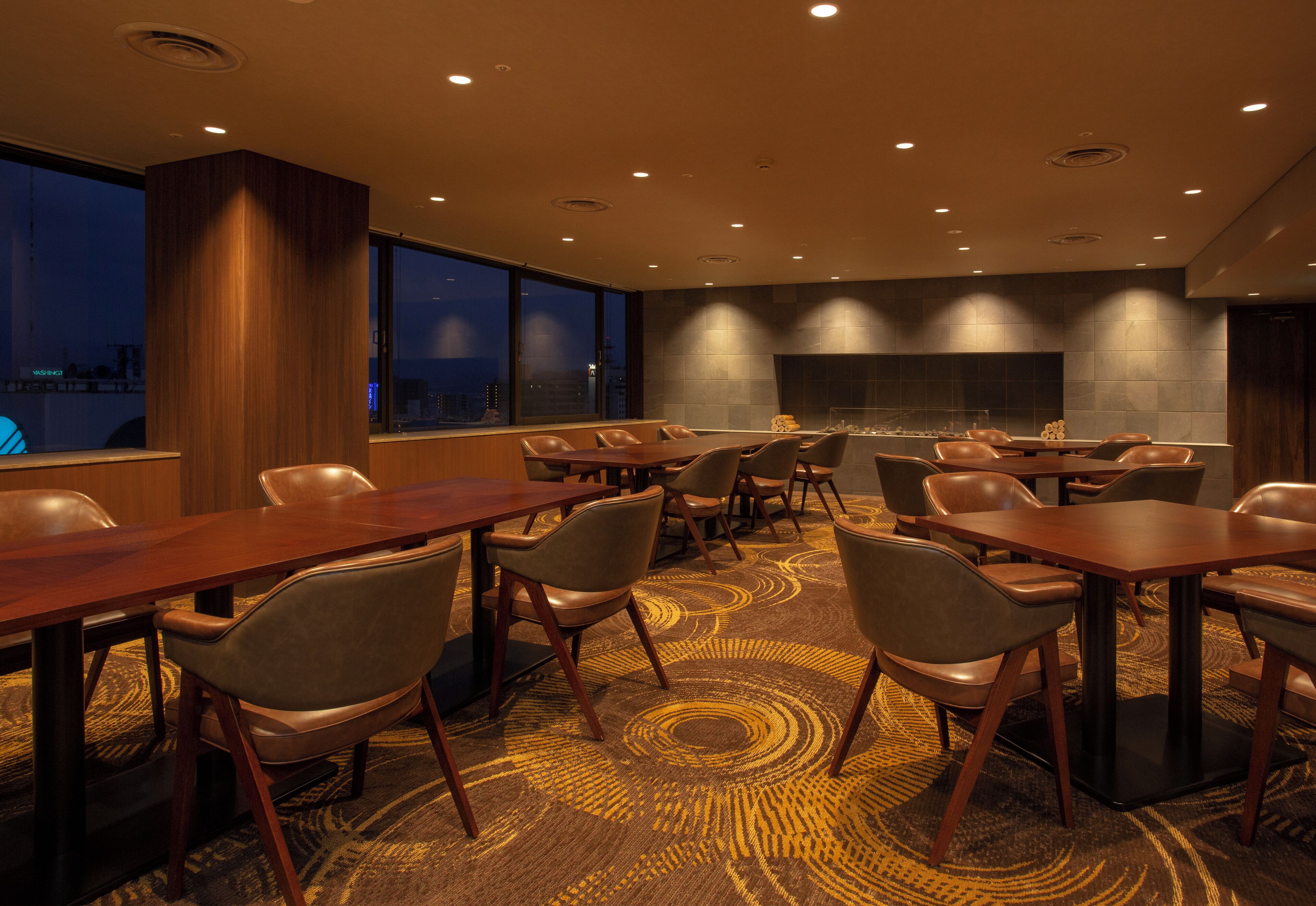 A conference room with multiple tables and chairs, large windows with a city view, and a fireplace.