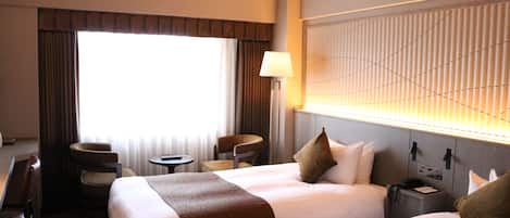 A hotel room with two beds, a desk, a chair, a lamp, and a window with curtains.