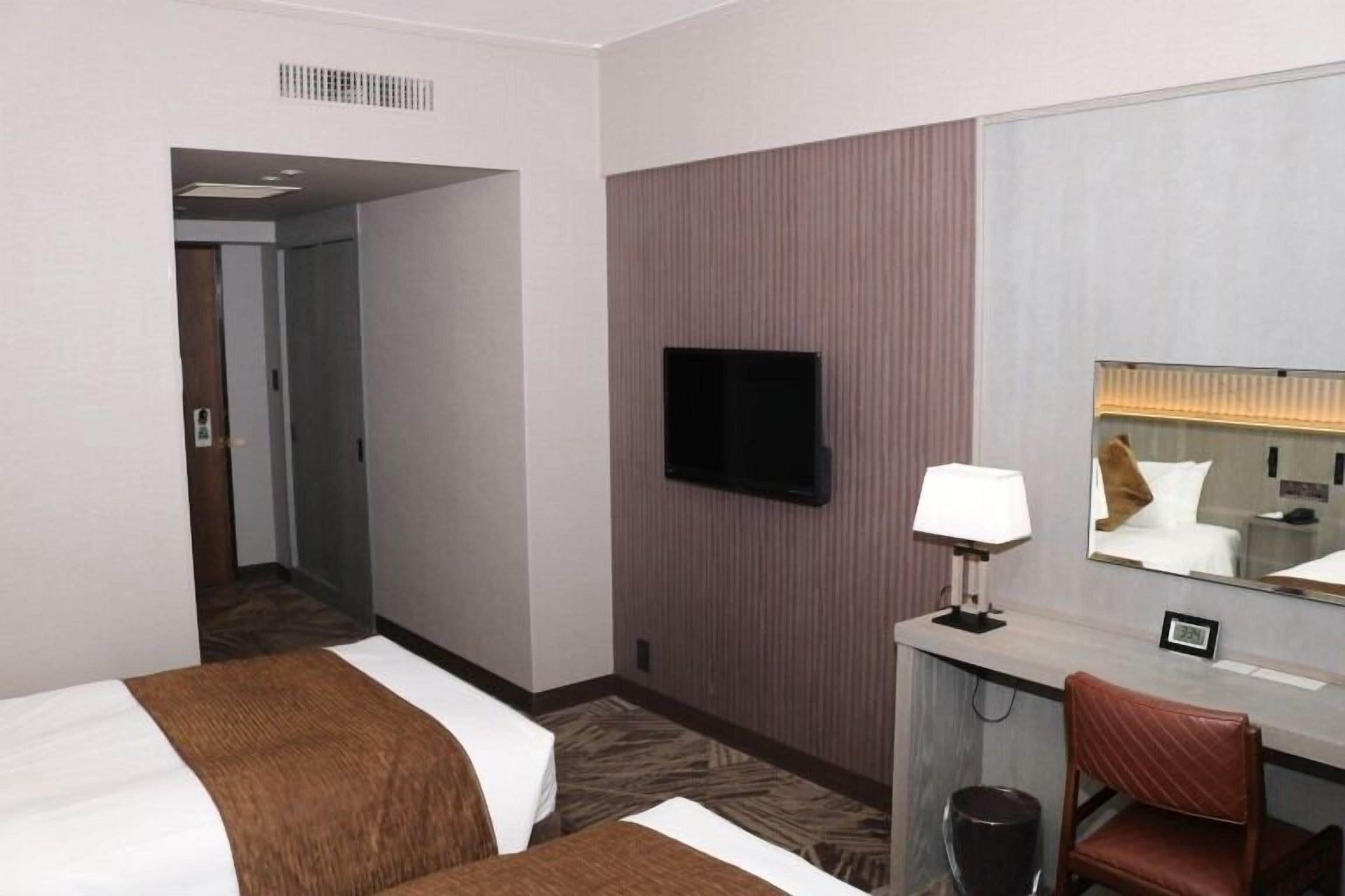 Habitación de hotel con dos camas, un escritorio, una silla, un televisor y un espejo.